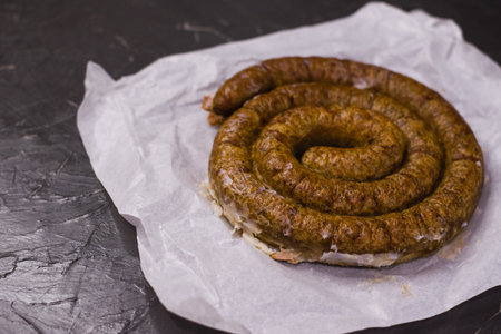 Delicious baked homemade sausage on non-stick baking paper on a dark background, preparation for celebrating Easter with the familyの写真素材