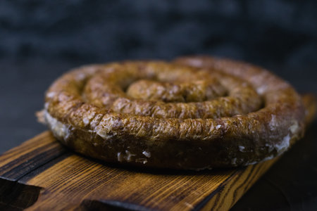 Delicious baked homemade sausage close-up on a dark wooden cutting board, on a dark concrete background, preparation for celebrating Easter in the family.の写真素材