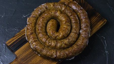 Delicious baked homemade sausage close-up on a dark wooden cutting board, on a dark concrete background, preparation for celebrating Easter in the family.の写真素材