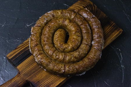 Delicious baked homemade sausage close-up on a dark wooden cutting board, on a dark concrete background, preparation for celebrating Easter in the family.の写真素材