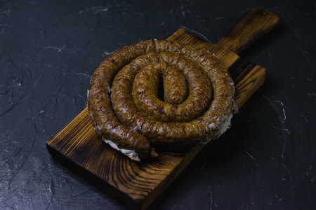 Delicious baked homemade sausage close-up on a dark wooden cutting board, on a dark concrete background, preparation for celebrating Easter in the family.の写真素材