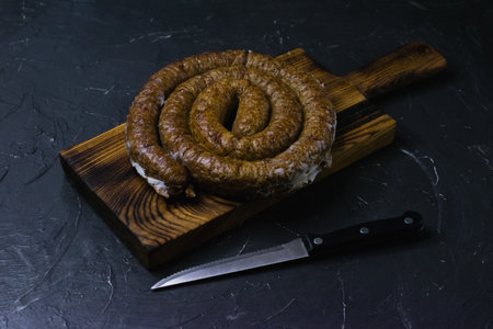 Delicious baked homemade sausage close-up on a dark wooden cutting board, on a dark concrete background, preparation for celebrating Easter in the family.の写真素材