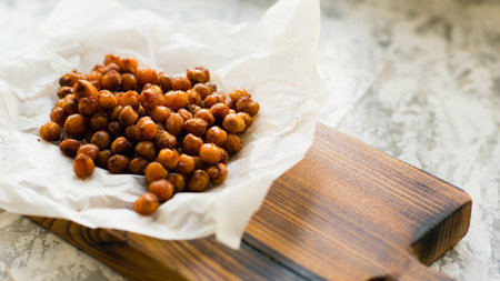 Delicious snack, baked chickpeas on baking paper on a wooden cutting board on a light table. Healthy eating conceptの写真素材