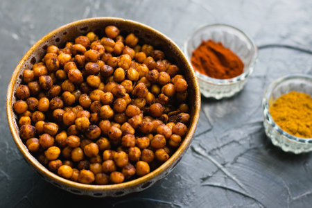 Delicious snack, fragrant baked with curry spices and smoked paprika chickpeas in a brown bowl and spices on a dark background with space for text. Healthy eating conceptの写真素材