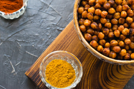 Delicious snack, fragrant baked with curry spices and smoked paprika chickpeas in a brown bowl and spices on a dark background with space for text. Healthy eating conceptの写真素材