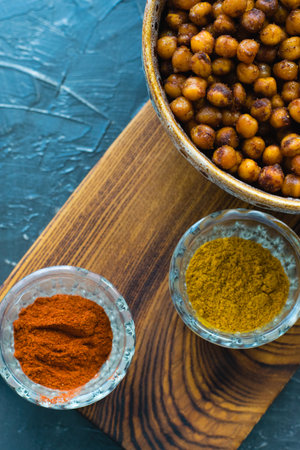 Delicious snack, fragrant baked with curry spices and smoked paprika chickpeas in a brown bowl and spices on a dark background with space for text. Healthy eating conceptの写真素材