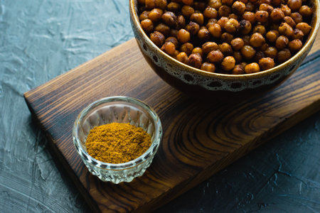 Delicious snack, fragrant baked with curry spices and smoked paprika chickpeas in a brown bowl and spices on a dark background with space for text. Healthy eating conceptの写真素材