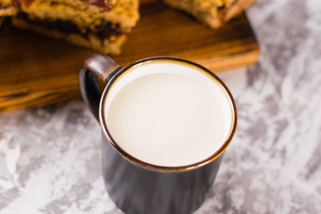 Delicious homemade pie with apple jam. Appetizing slices of grated pie with jam on a wooden board and a cup of milk on a light table.の写真素材