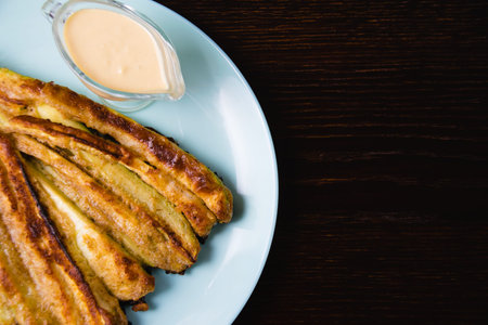 Delicious fried zucchini with aromatic sour cream garlic sauce on a plate on a dark table