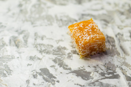 Sweet pumpkin dessert. A cube of pumpkin marmalade and coconut flakes on a light background with space for textの写真素材