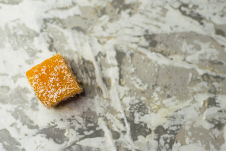 Sweet pumpkin dessert. A cube of pumpkin marmalade and coconut flakes on a light background with space for textの写真素材