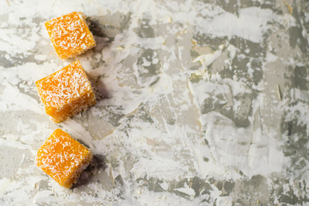 Sweet pumpkin dessert. Cubes of pumpkin marmalade and coconut flakes on a light background with space for textの写真素材