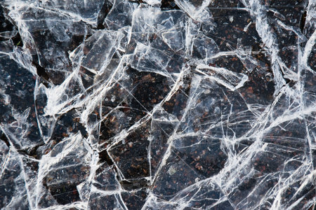 Cracked ice close-up. Frozen water, ice on dark asphalt.