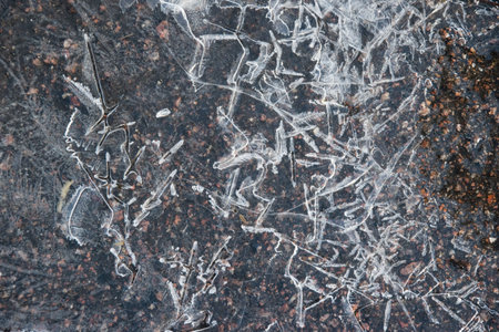 Cracked ice close-up. Frozen water, ice on dark asphalt.