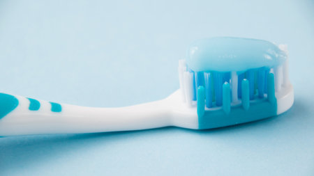 Blue toothbrush with toothpaste close-up macro on light background.