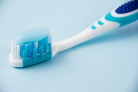 Blue toothbrush with toothpaste close-up macro on light background.