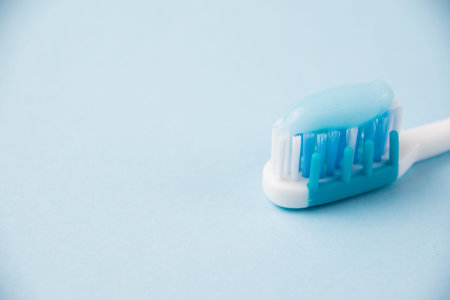 Blue toothbrush with toothpaste close-up macro on light background.
