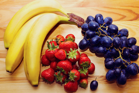 Still life of natural fresh fruit. Bananas, strawberries and blue grapes on the table.の写真素材