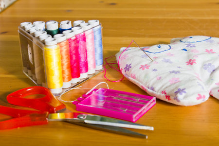 Sewing kit on a wooden table. Thread, needles, scissors and a toy on the table.