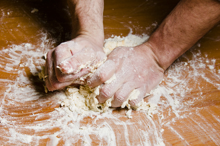 Men's hands knead the dough on the wooden table. The chef prepares the dough for Italian cuisine.の写真素材