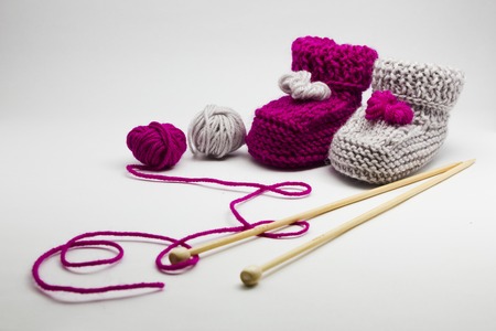 Couple knitted bootees to newborn, knitting needles and balls of yarn isolated on white background. Hand-made socks for the baby.の写真素材
