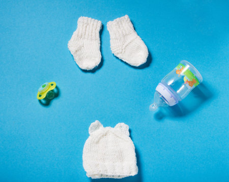 Knitted by hands wool white hat and socks for the newborn. Winter hand made clothing for the child on blue paper background. Hobbies for Women: knitting.の写真素材