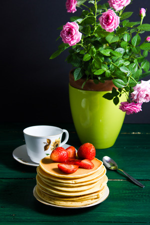 Traditional breakfast: pancakes with syrup and strawberry, green tea. Still life, served on green wooden table.の写真素材