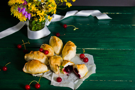 Traditional Russian cuisine: cakes with sour cherries. Still life with cakes and a vase with flowers on a green wooden table in rustic style.の写真素材