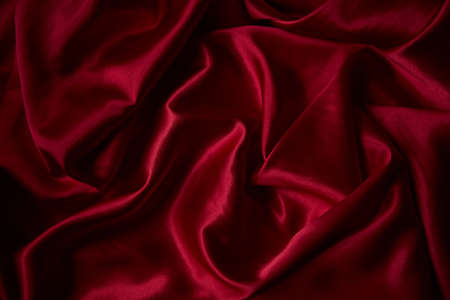 Beautiful draped silk fabric in red. Background from the waves of satin fabricの写真素材