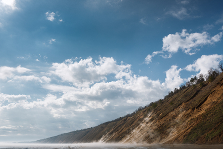 a misty spring morning on the snowy shore of a calm river overlooking the mountainsの写真素材