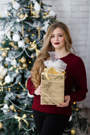 Happy young lady with long hair gifts by the fireplace near the Christmas treeの写真素材