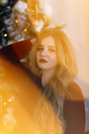Happy young lady with long hair gifts by the fireplace near the Christmas treeの写真素材