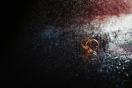 Wedding rings on dark surface shining with light close up macro. Water splashes. Reflection. Lights and smoke. Pair Ringの写真素材