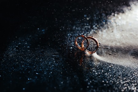 Wedding rings on dark surface shining with light close up macro. Water splashes. Reflection. Lights and smoke. Pair Ringの写真素材