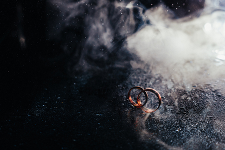 Wedding rings on dark surface shining with light close up macro. Water splashes. Reflection. Lights and smoke. Pair Ringの写真素材