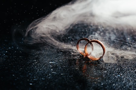 Wedding rings on dark surface shining with light close up macro. Water splashes. Reflection. Lights and smoke. Pair Ringの写真素材