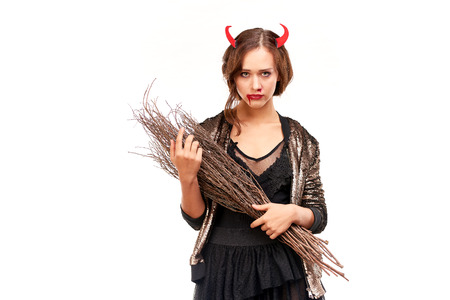 Portrait of beautiful she-devil posing with broom on Halloween against white backgroundの写真素材