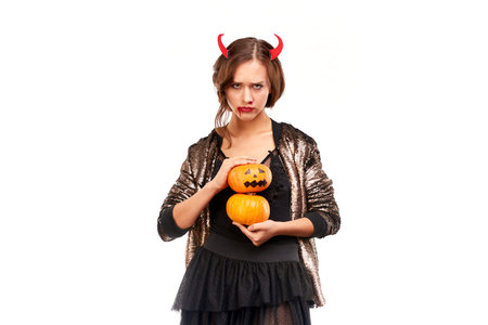 Portrait of beautiful she-devil posing with jack-o-lanterns on Halloween against white background