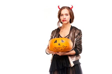 Portrait of beautiful she-devil posing with jack-o-lantern on Halloween against white backgroundの写真素材