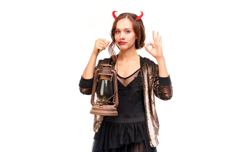 Portrait of beautiful she-devil posing with lantern on Halloween against white backgroundの写真素材