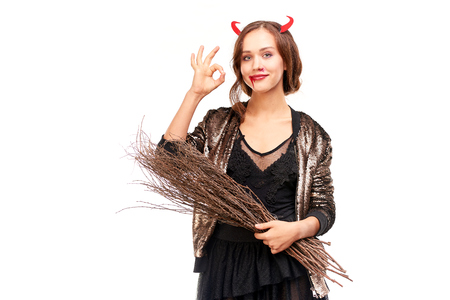 Portrait of beautiful she-devil posing with broom on Halloween against white backgroundの写真素材