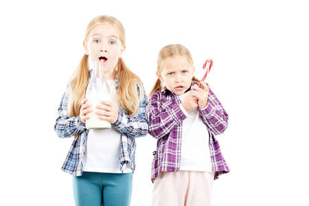 Studio portrait of two little sisters holding bottle of milk and candy caneの写真素材