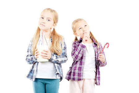 Studio portrait of two little sisters holding bottle of milk and candy caneの写真素材