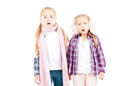 Portrait of two little sisters wearing scarf and earmuffs posing against white backgroundの写真素材