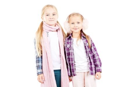 Portrait of two little sisters wearing scarf and earmuffs posing against white backgroundの写真素材