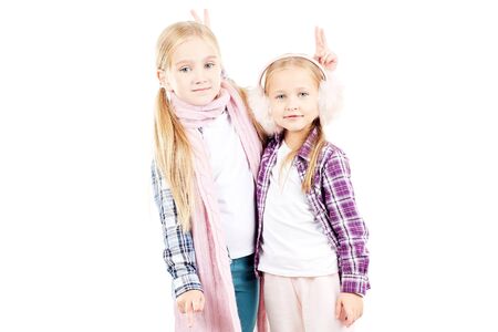 Portrait of two little sisters wearing scarf and earmuffs posing against white backgroundの写真素材