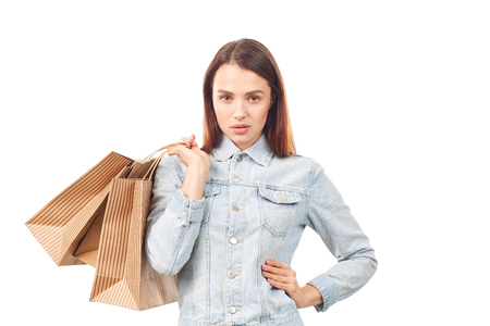 Portrait of young woman in denim jacket holding shopping bags on white backgroundの写真素材