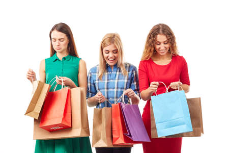 Portrait of three young girlfriends holding bunches of multi-colored shopping bagsの写真素材