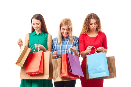 Portrait of three young girlfriends holding bunches of multi-colored shopping bagsの写真素材