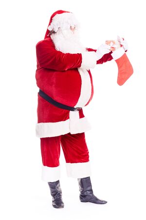 Portrait of Santa Claus hiding gift box into Christmas stocking on white backgroundの写真素材